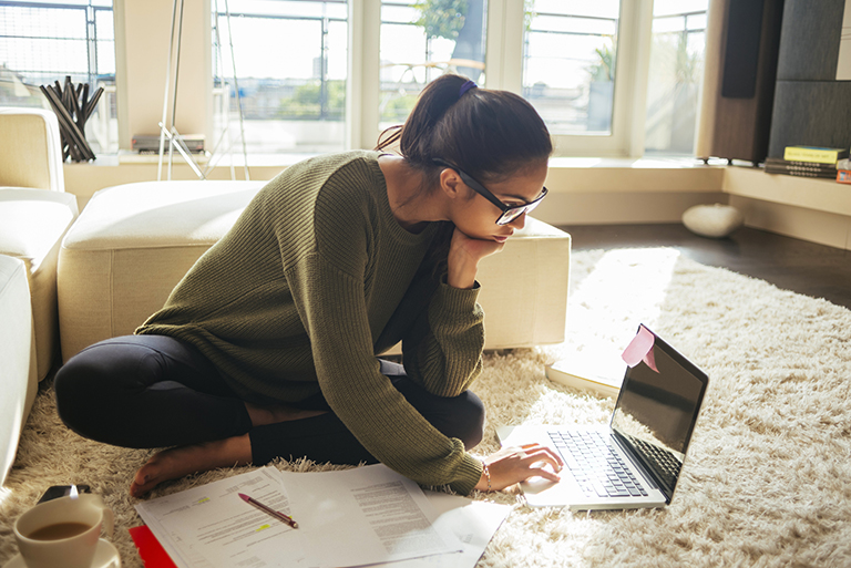 young woman studying and working on her laptop,sitting on the carpet in the living room,nice sunny day