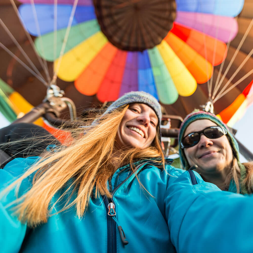 Two women taking a selfie with a hot air balloon in the background