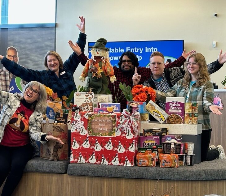 GNCU employees posing for a photo surrounded by food donations for the Greater Giving Holiday Donations Drive.